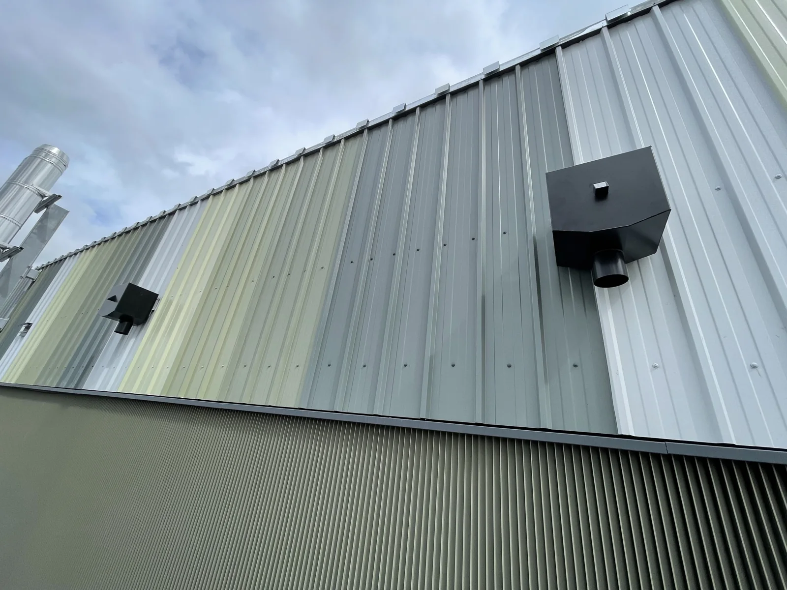 Profiled metal cladding and rainwater hoppers under an overcast sky